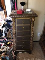 Front view of tall wood jewelry stand with six drawers and gold leaf accents on edges and corners. Several items on top but not included.