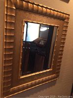 Front view of gold framed wall mirror showing detailed textured gold frame and reflective surface.