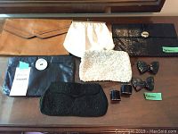 Six vintage clutch purses including leather, beaded, and python styles and two sets of shoe clips, arranged on table