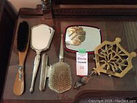 Full view of all items: wooden hairbrush, sterling silver hand mirror, nail buffer, hairbrush, and brass trivet with wooden handle.