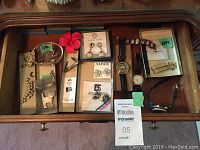 Top view of jewellery and items in display drawer showing assorted earrings, necklaces, vintage pocket knife, and watches.