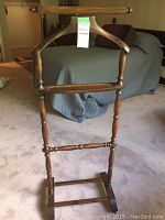 Full view of a wooden clothing valet stand with shaped hanger and turned legs.