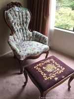 Full view of mahogany upholstered chair with floral fabric upholstery and needlepoint ottoman in front.