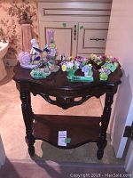 Dark wood half moon table with bone china floral figurines displayed on top, showing overall setup and condition of table and items.