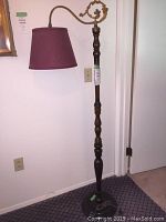 Full view of antique cast arm bridge floor lamp with turned mahogany pole, curved arm and burgundy shade.