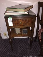 Full view of mahogany side table with three books stacked on glass top and two photo frames on lower shelf