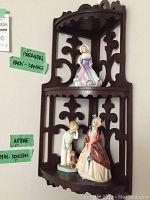 Overall view of the dark wooden corner shelf with three figurines displayed on it. Green tape notes indicate damage on the Paragon figurine at the back and information on Artone and Royal Doulton figurines.