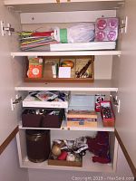 Photo of cabinet shelves containing knitting needles, boxes with thread, wooden tools and various sewing accessories.