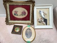 Four assorted framed artworks grouped together on floor showing embroidery, silhouette, illustration, and print with varied frames