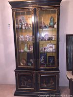 Full front view of the Oriental style china cabinet with glass doors showing decorative items inside and painted scenes on the lower doors.