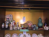 Shelf display with assorted Asian pottery, ceramics, and decorative items including vases, jugs, and small cups.
