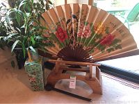 The large silk folding fan displayed on a wooden stand with the blue-green oriental vase and plant on the left side. Gong mallet is visible in front of the stand. Photos taken to show the full set, art detail on fan, and decorative vase with plant.