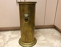 Full front view of tall cylindrical brass umbrella holder with lion head ring detail, showing the patina and form.