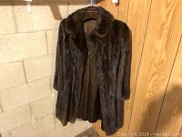 Full view of dark brown mink fur jacket hanging on a hanger, showing length, sleeves and collar.