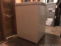 Side and front view of the small white deep freeze chest freezer showing its rectangular shape and flat lid with some surface marks.