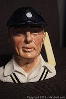 Close-up image of Royal Doulton figurine showing the front of the cricketer's face with detailed facial features, navy blue cricket cap with emblem, and bat over the shoulder.