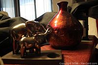 Photo showing metallic elephant candle holder with two elephants on a rectangular base and burgundy/gold vase with a rounded body and narrow neck.