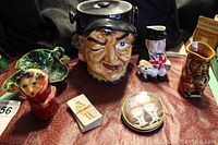 Full lot view showing the cigar chewing man cookie jar, small figurines, pottery jugs, John Player & Sons collector cards, and a small tray.