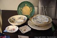 Various decorative plates including large green plate with gold pot design, floral bowl, small floral and lattice plates, and metal plate stands.