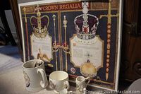 Framed print showing Crown Regalia with detailed images of crowns and explanatory text. Cups and egg cup placed in front.