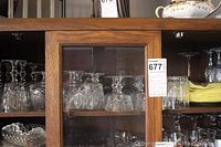 Wooden cabinet shelf with multiple clear glass stemware including old fashioned glasses and flutes