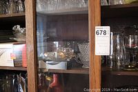 Glass miscellaneous bowls, trays, cream and sugar sets on wooden shelving behind glass doors