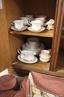 Image showing teacups and saucers on wooden shelf with white porcelain rabbit figurine