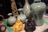 Four small Asian design vases in green hues, two Buddha figurines in orange and dark brown, placed on a surface