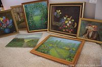 Full view of seven original framed and unframed acrylic paintings arranged upright and leaning, mostly floral and landscape themes.