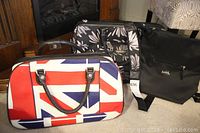 Three bags shown together: a black Tracker floral carry on bag, a British flag design carry on bag, and a black Inniskillin cooler bag.