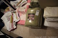 Pink and cream quilt, green double size ultra lux blanket in packaging, stacked linens and pillowcases.