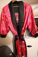 Reversible kimono robe side with vibrant pink floral pattern, black collar and cuffs, hanging on hanger.