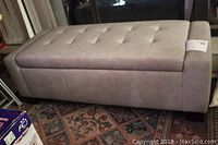Front view of light grey padded storage bench showing tufted top and block feet
