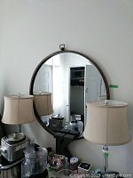 Front view of a large round mirror on wall, showing reflection of lamps and room interior.