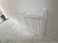 Full view of the white metal safety gate mounted in a doorway against a white wall and tiled floor.
