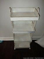 Front view of a 4-tier white distressed shelving unit showing tray-like shelves with raised edges and rounded vertical side handles.