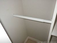 Close-up of a white metal hanging rod installed in the closet corner.