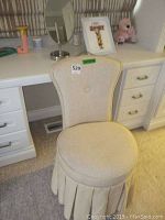 View of beige upholstered vanity chair with rounded back and button tuft, placed next to white desk
