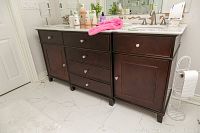 Front view of entire vanity showing dark wood cabinet, white marble top, two undermount sinks and brushed nickel faucets