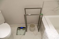 View of the four bathroom items together: scale, toilet paper holder, towel rack, and waste basket on bathroom floor near toilet and bathtub.