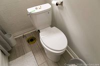 White Toto toilet installed in a corner bathroom with floor tiles and white walls, showing the full toilet and floor flange.
