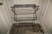 Front view of folded metal drying rack showing multiple horizontal bars for drying clothes.