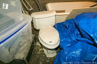 Overview of toilet bowl, tank and seat surrounded by storage items