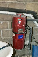 Front view of red Vacuum King Ltd. central vacuum unit mounted on concrete basement wall with connected pipes.