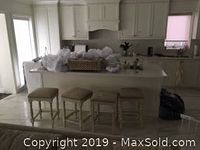 Overall view of white kitchen island with three matching stools in room setting