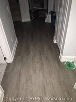Hallway floor installed with vinyl planks, showing a grayish wood finish in a corridor with white baseboards.