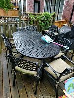 Wide shot of black lattice metal table and ten matching chairs with beige cushions on deck