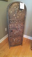Front view of full decorative metal wine rack with embossed grapevine design and ornamental scrollwork, wooden floor background.