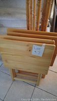 Four wooden TV trays stacked together, showing light wood color and folded legs