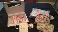 Closed silver metal case with manicure tools inside, placed beside two cosmetic bags - one floral wrapped in plastic and one leopard print.